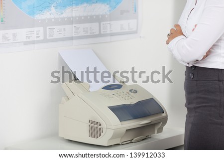 Midsection of businesswoman using fax machine in office