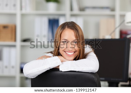 Portrait of happy young businesswoman leaning on chair in office