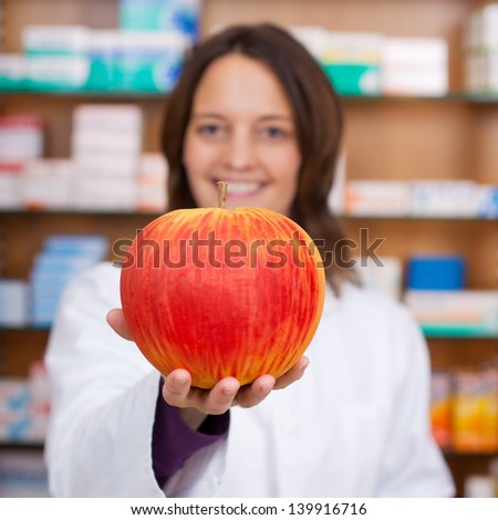 Portrait of confident female pharmacist holding artificial apple in pharmacy