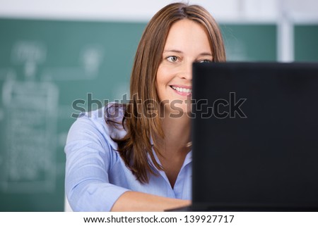 Mid adult female teacher using laptop against chalkboard in classroom