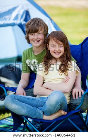 Portrait of young brother and sister sitting together on chair with tent in background