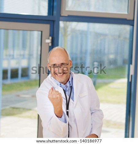 Portrait of happy male doctor clenching fist while celebrating victory in clinic