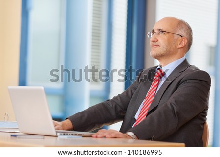 Thoughtful businessman with laptop looking up at office desk
