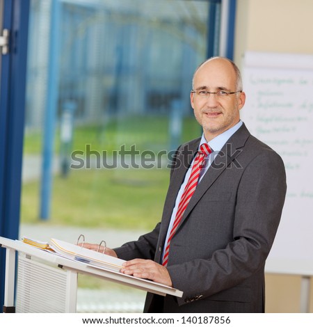 Portrait of confident mature businessman standing at podium in office