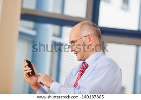 Mature businessman touching cell phone screen in office