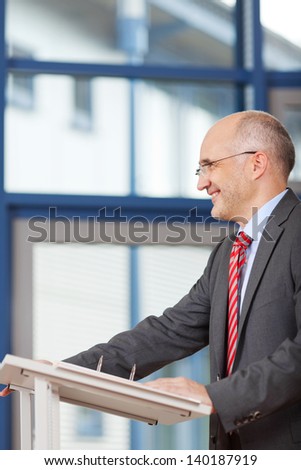 Side view of mature businessman standing at podium in office