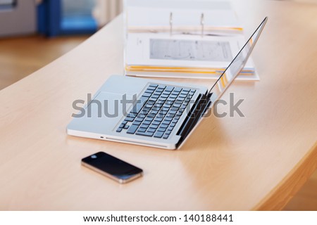 Mobile phone; laptop and binder on wooden desk in office