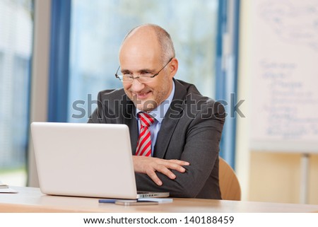 Happy mature businessman looking at laptop at office desk