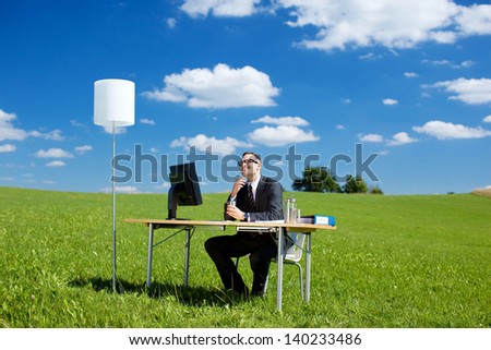Smiling businessman working with computer and table in green meadow
