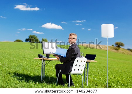 Businessman working with folder and computer in green meadow