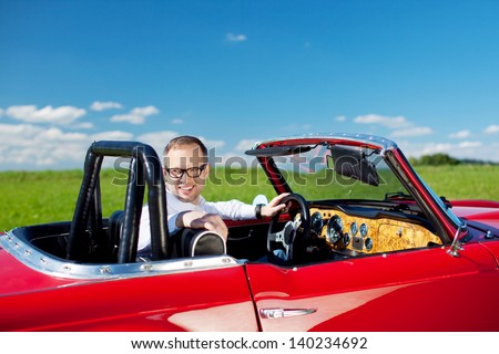 Happy man relaxing in his stylish red cabriolet in lush open countryside looking back at the camera