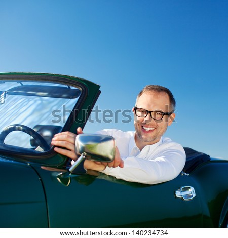 Closeup portrait against blue sky of a happy man driving a cabriolet leaning over to look at the camera