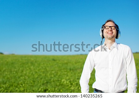 Man relaxing listening to music on headphones in a lush green field standing with his head tilted back to the sun
