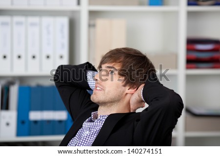 Relaxed young businessman with hands behind head looking up in office