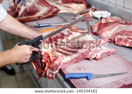 A butcher cutting the ribs of sheep carcass using the saw