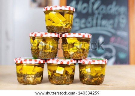 Jars with gourmet white cheese cubes and herbs dipped in olive oil in a grocery