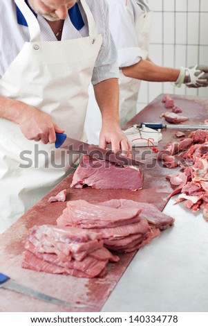 Butcher cutting meat on a long chopping board slicing off portions of steak for sale in the retail market
