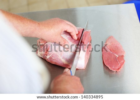 Close-up of butcher hands holding a knife slicing thin stakes over a stainless steel workbench