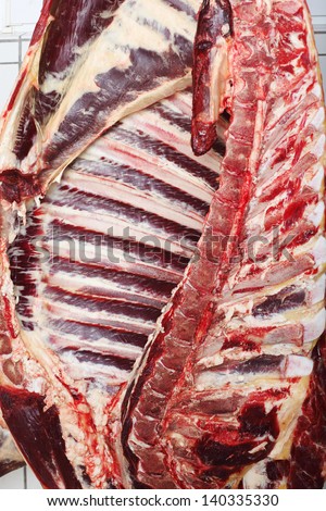 Half of a freshly cut cow carcass showing the ribs and spine, hanging on a butcher