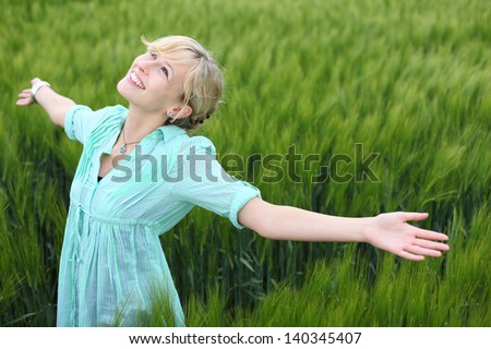 Pretty woman rejoicing in a green field standing with her arms spread wide open enjoying the beauty and tranquillity of nature