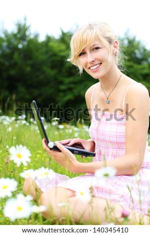Attractive natural young blond woman sitting with her laptop amongst white spring daisies in a rural meadow