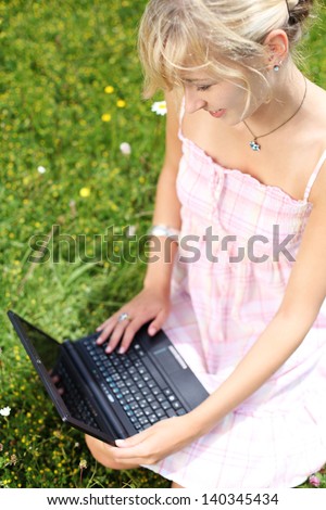 High angle view looking down n the keyboard of a young woman kneeling in a grassy meadow working on her laptop in nature