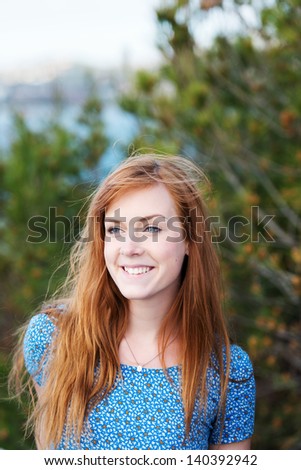 Smiling young redhead woman with tousled hair, head and shoulders portrait in nature