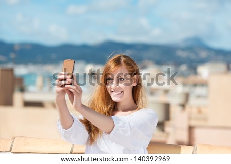 Smiling woman taking her photograph using a mobile phone and smiling as she poses for the picture