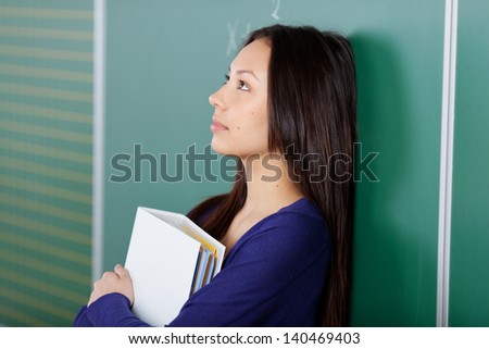 female student leaning against blackboard looking up thoughtful