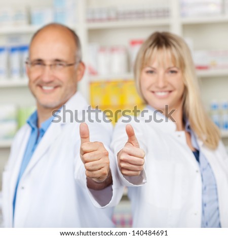 Portrait of male and female pharmacists showing thumbs up in pharmacy