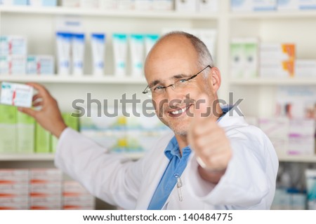 pharmacist showing thumbs up sign while taking medicine from shelf in pharmacy