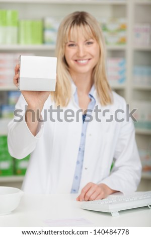 Portrait of young female pharmacist showing medicine box at pharmacy counter