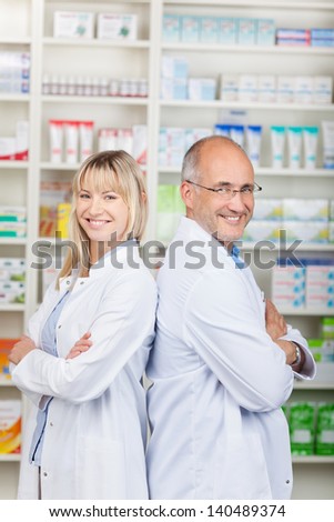 smiling pharmacists standing back to back with crossed arms