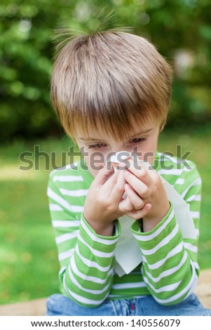 Little boy blowing his nose because of allergy in the garden
