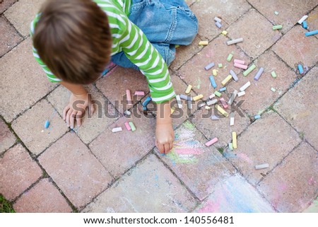 Young little boy drawing on the pavement using colorful chalk