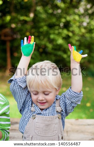 Looking boy raising his colorful painted hands