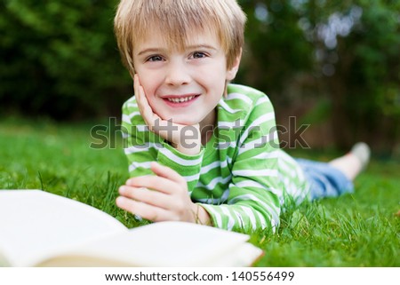 Cheerful little boy reading book on the grass