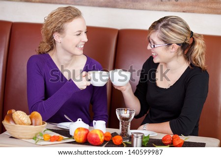 Happy female friends toasting coffee cups at cafe table