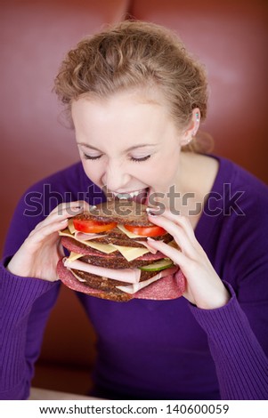 Young woman biting big burger at coffee shop