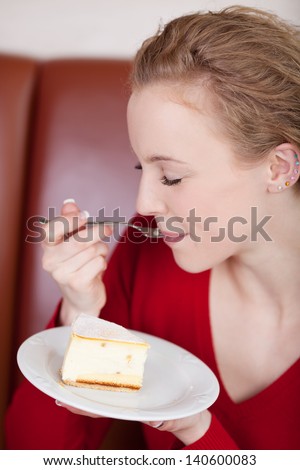 blond woman enjoying cheese cake in a coffee house