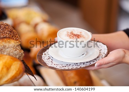 saleswoman passing cappuccino over the counter in a bakery