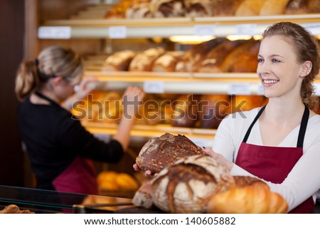 saleswoman in bakery with bread in her hands in front of shelves