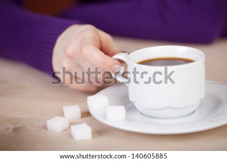 Closeup of female customer\'s hand with coffee cup and sugar cubes at wooden table