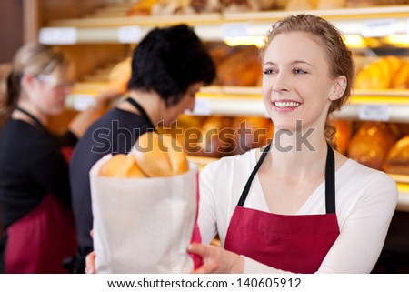 smiling saleswoman in bakery passing bag of breads