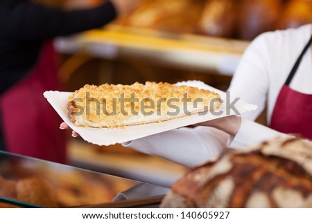 Closeup of female bakery worker holding tray of sweet bread at counter