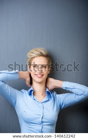 Smiling young woman with hands behind head resting against blue wall
