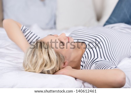 Thoughtful young woman with hands behind head lying on bed