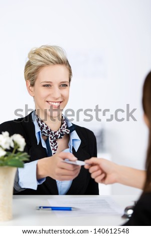 Happy young businesswoman receiving cardkey from receptionist at reception