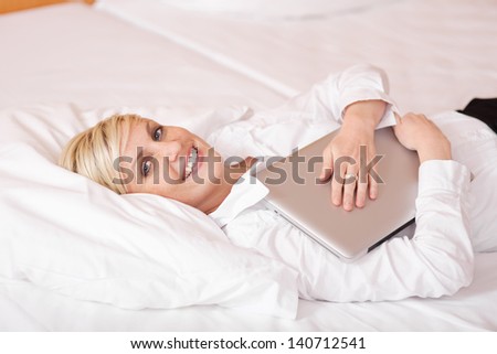 Happy businesswoman with laptop lying on bed