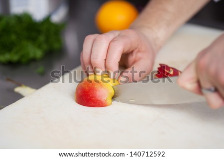 Closeup of chef\'s hands cutting an apple on chopping board in commercial kitchen